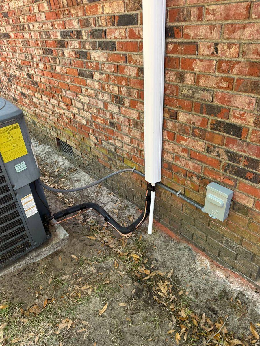 Close view of the relocated condenser: insulated line set, drain line and electrical disconnect neatly routed along a brick wall