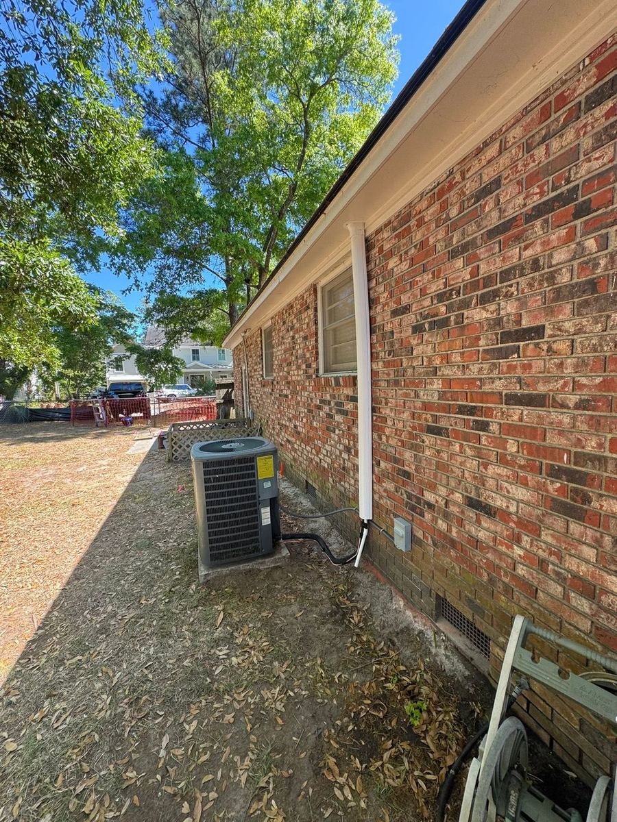 Relocated condenser beside a brick home in Charleston, line set run in a white cover up the wall